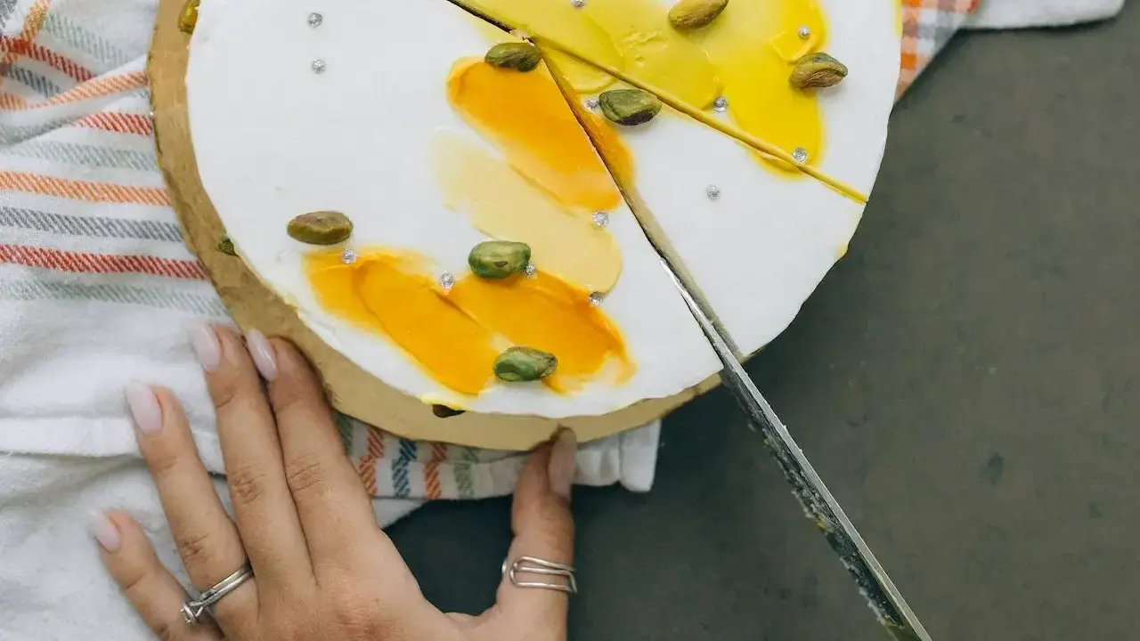 Delikatny tort z pistacjami i żółtym kremem, pokazany w momencie, jak kroić tort.