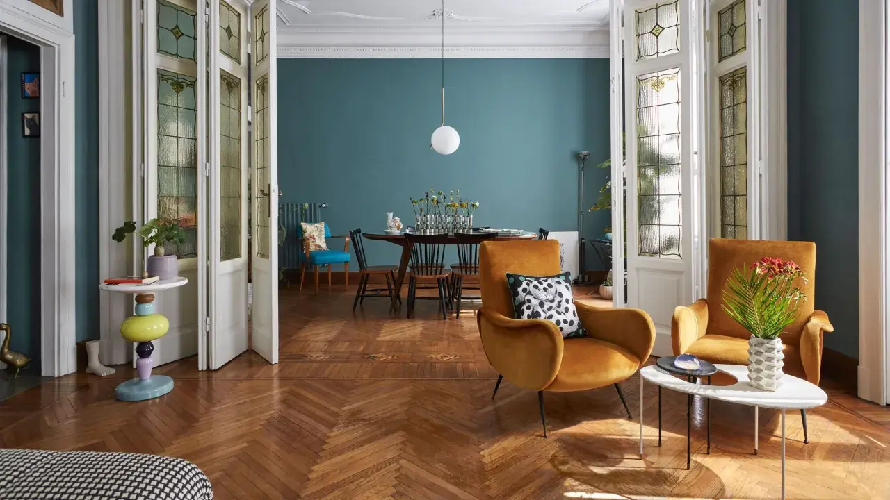 Un soggiorno che unisce con successo arredamento classico e moderno: sedie in velluto ocra, tavolino di design e porte antiche con vetri colorati.