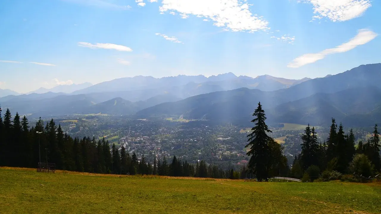 Widok z Gubałówki na Butorowy Wierch i Tatry. Słoneczny dzień, chmury na niebie.