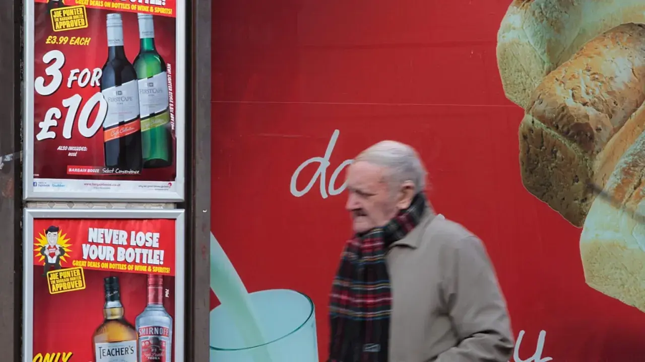 Starszy mężczyzna mija reklamę z promocją na alkohol. Włochy ceny alkoholu są atrakcyjne.
