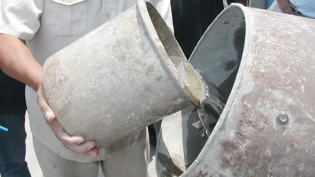 Se vierte agua de un cubo a otro, preparándose para proporcionar cemento y agua.