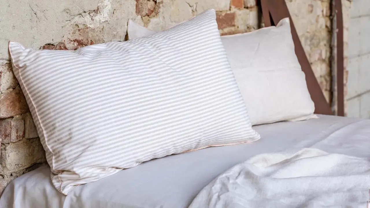 Cuscini a righe e tinta unita su un letto coperto da lenzuola di lino. Le caratteristiche del linone tessuto sono evidenti nella texture naturale.