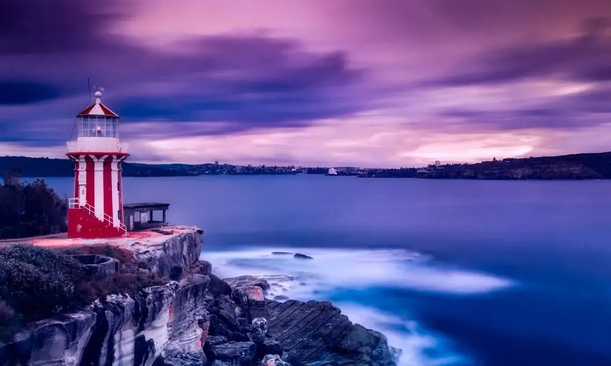 Kolorowa latarnia morska rysunek dla dzieci, stojąca na klifie, z falami rozbijającymi się o skały.