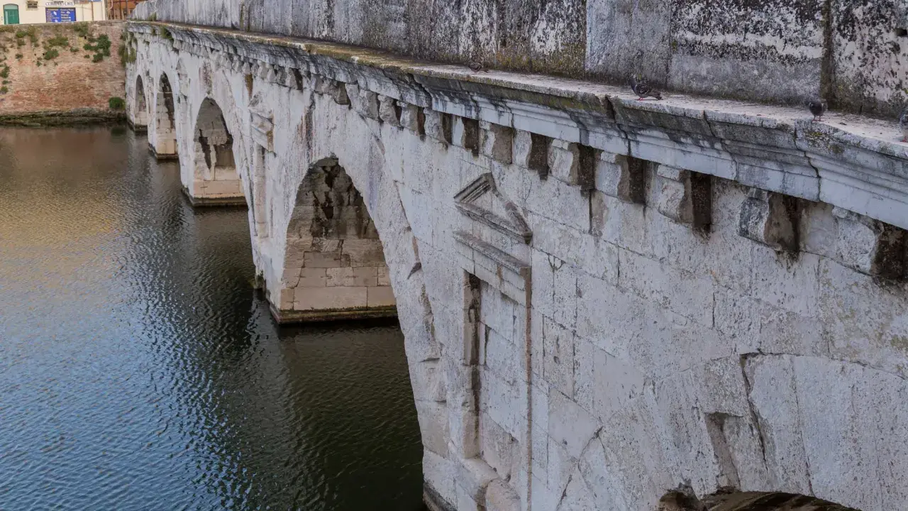 Il Ponte di Tiberio a Rimini, con i suoi archi in pietra bianca che si specchiano sull'acqua scura, testimonia secoli di storia.