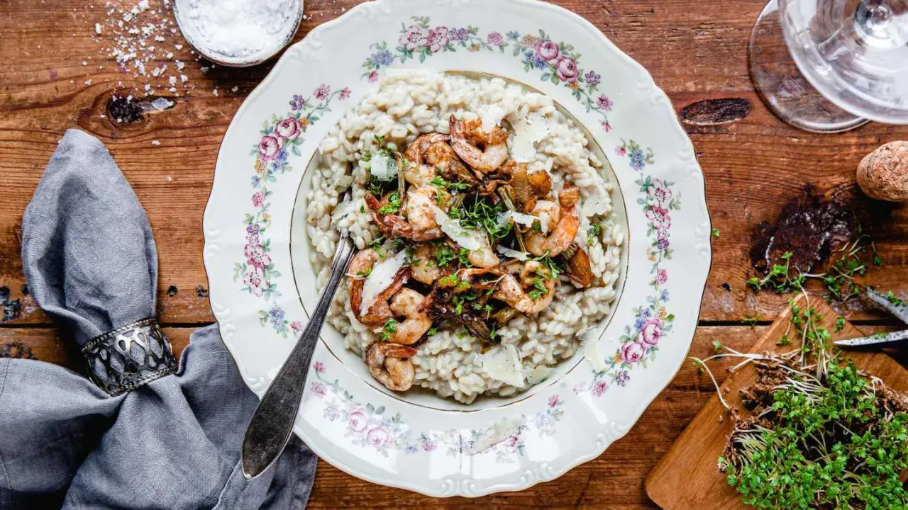 En tallrik med lyxig risotto toppad med räkor och svamp, serverad på ett vackert mönstrat fat.