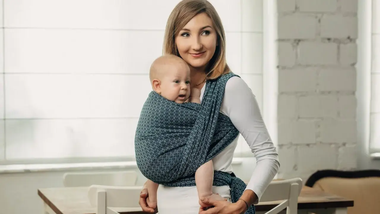 Uśmiechnięta mama nosi dziecko w chuście tkanej, która zapewnia komfort i bezpieczeństwo.