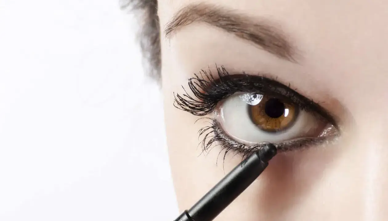 Ojo marrón recibiendo el toque final de maquillaje ojos negro con un lápiz.