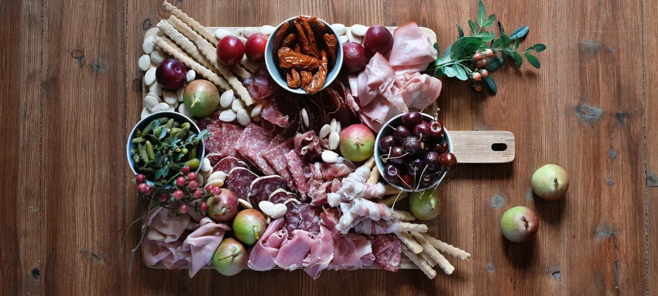 Tagliere con salumi tipici lombardi, frutta, sottaceti e grissini su un tavolo di legno.