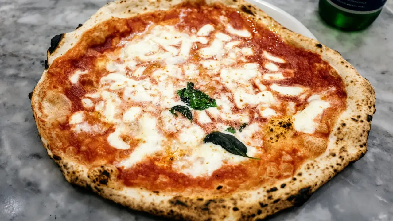 Pyszna pizza napoletana z rozpływającym się serem mozzarella i aromatycznym sosem pomidorowym, ozdobiona świeżą bazylią.