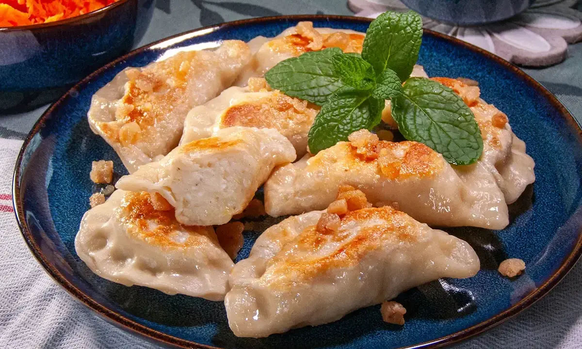 Pyszne pierogi ruskie przepis na talerzu, posypane skwarkami i udekorowane miętą.