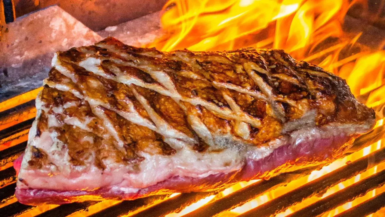 Jugosa viande de kobe a la parrilla, con marcas doradas y llamas naranjas danzando alrededor.