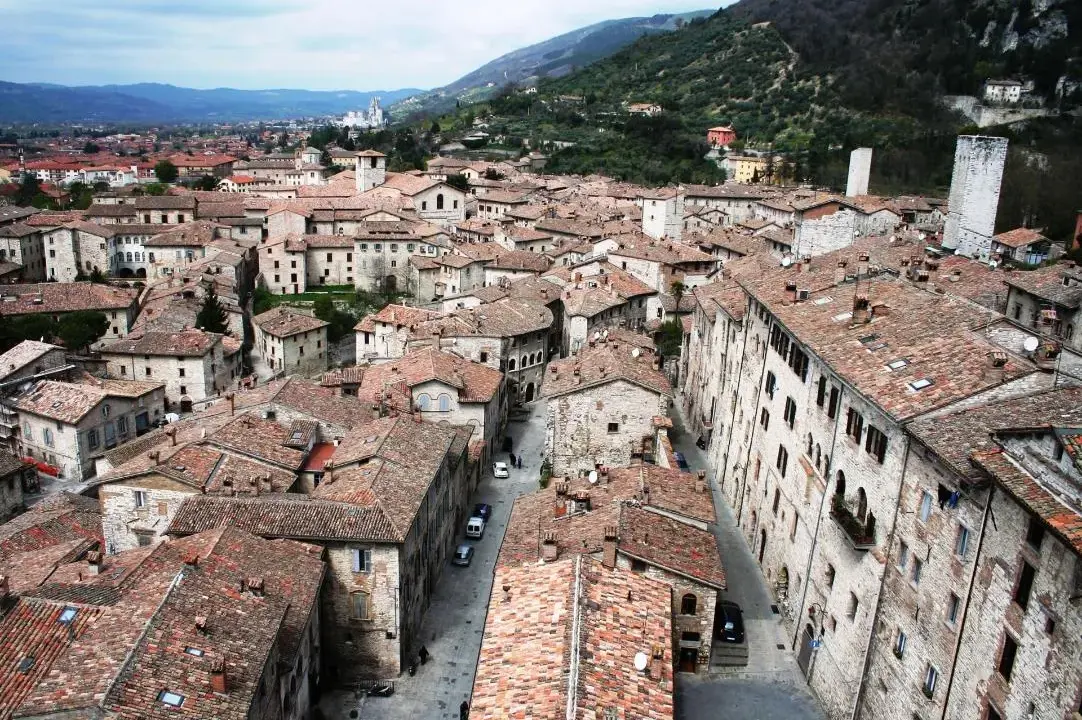 Panoramica di tetti rossi e antichi edifici in pietra, con torri medievali che svettano. Un paesaggio che ricorda l'Umbria, tra Assisi e Gubbio.