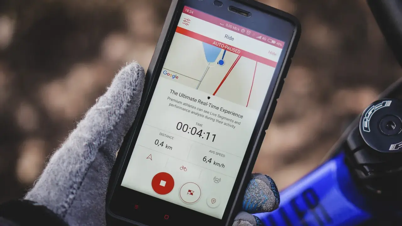 Rękawiczka trzyma smartfon z aplikacją licznik rowerowy. Widoczny czas 00:04:11, dystans 0,4 km i średnia prędkość 6,4 km/h.