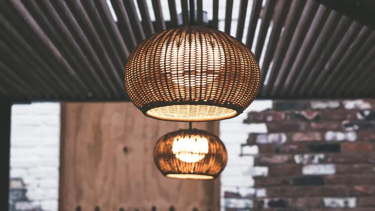 Dos lámparas de mimbre esféricas cuelgan bajo un techo de listones. La luz cálida que emiten crea un ambiente acogedor, con unos lumenes por m2 perfectos para relajarse.