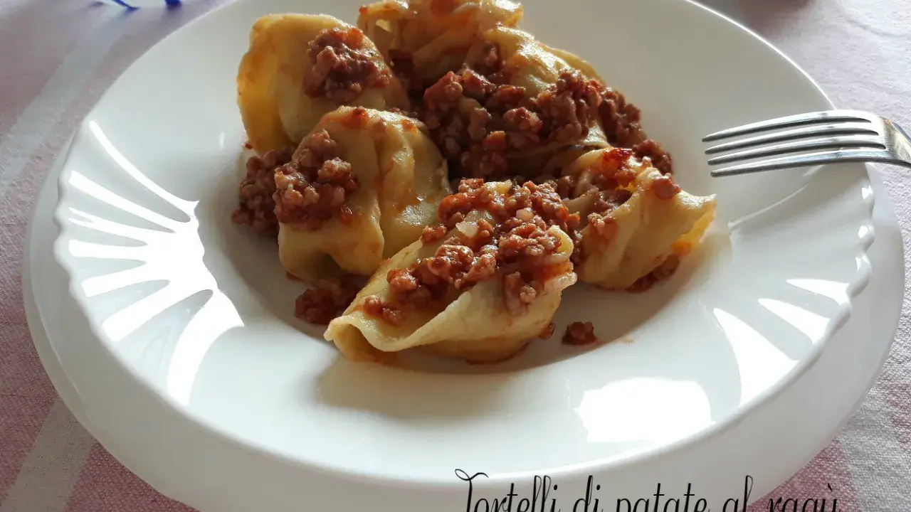 Tortelli di patate al ragù, un piatto gustoso e confortante, servito su un piatto bianco con una forchetta.