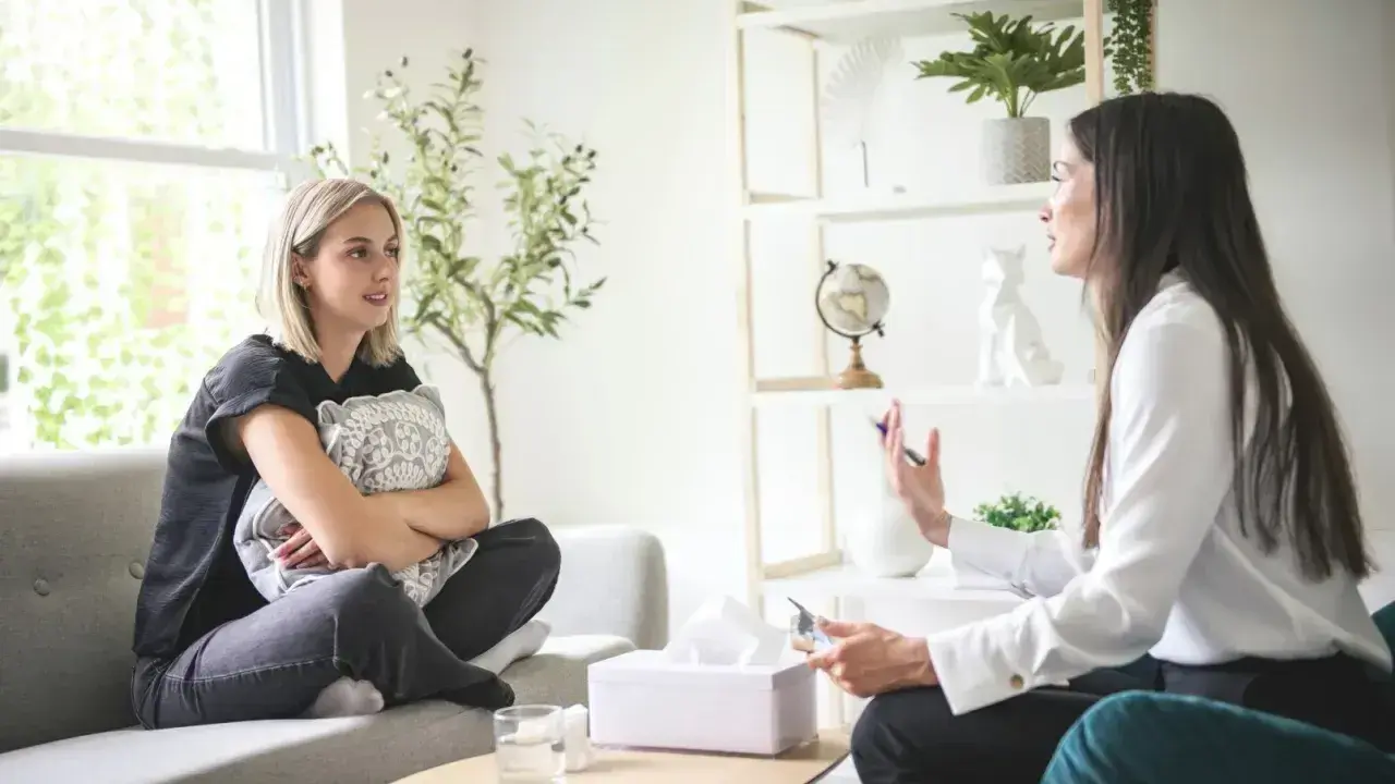Rozmowa terapeutyczna. Młoda kobieta z poduszką szuka odpowiedzi, jak zostać psychoterapeutą, słuchając uważnie specjalistki.