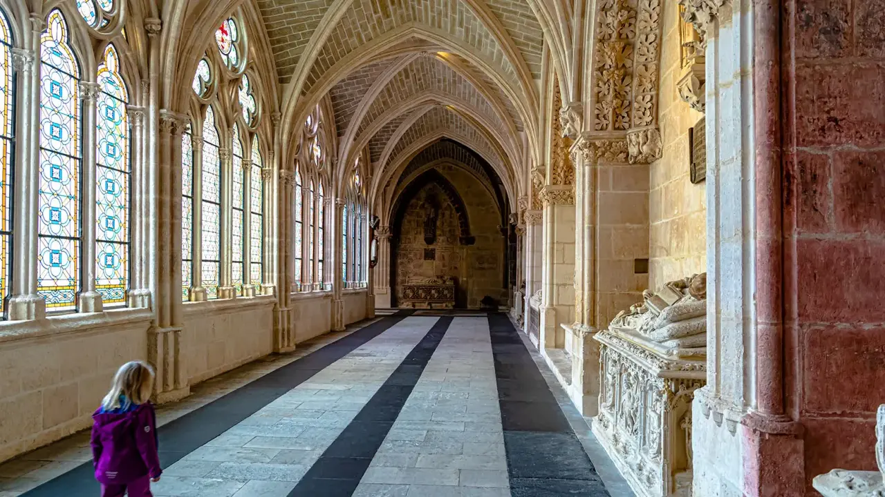 Ein Kind erkundet die gotischen Gänge der Burgos Kathedrale, vorbei an bunten Glasfenstern und kunstvollen Sarkophagen.