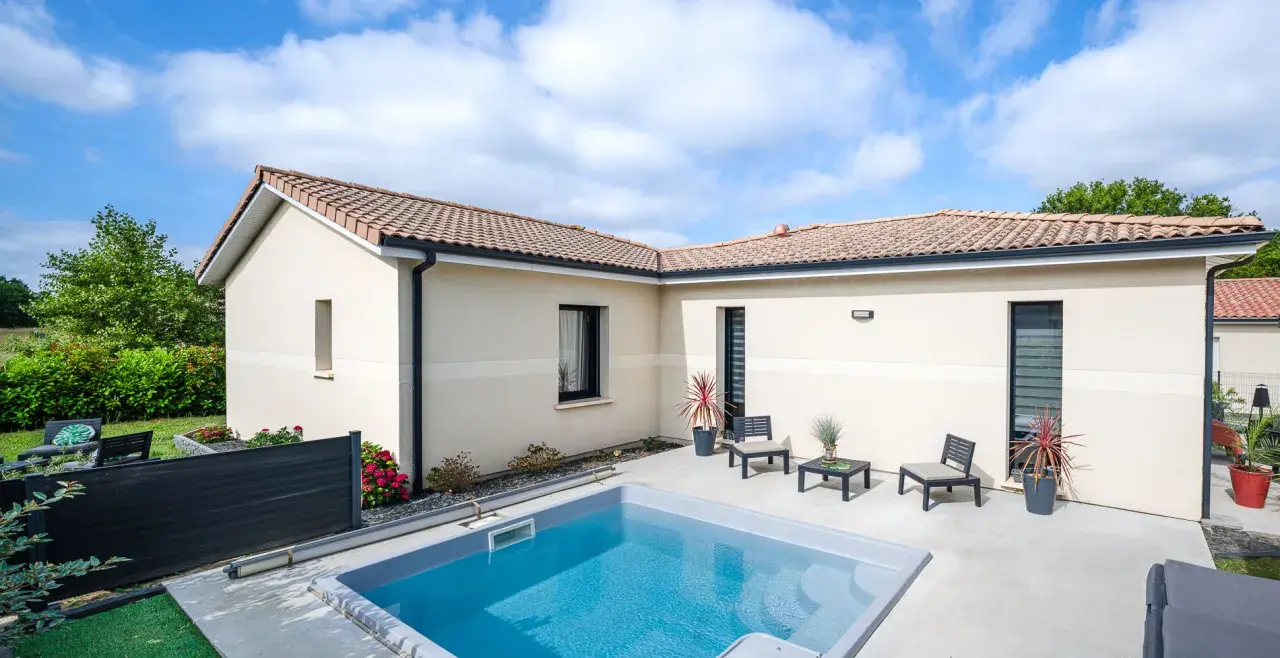 Vue aérienne d'une maison moderne avec piscine, le **plan maison en L** est bien visible, entouré de verdure.