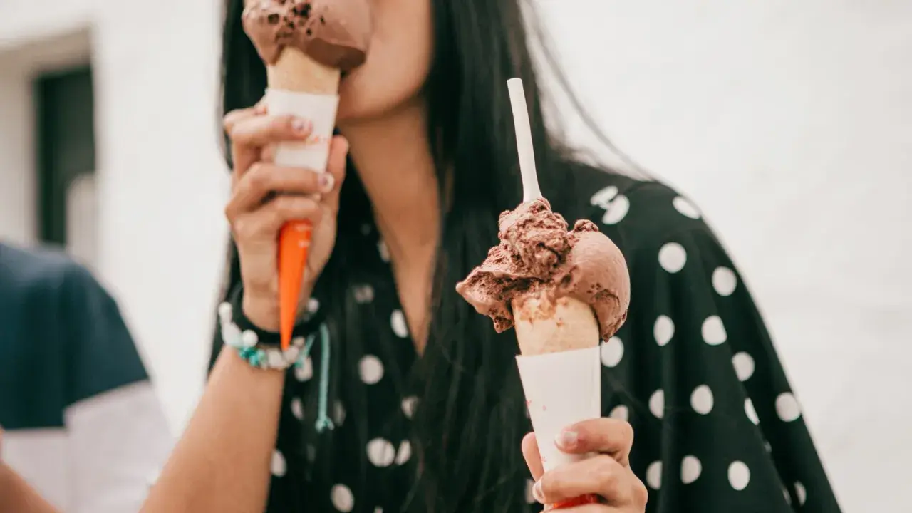 Una mujer disfruta de dos helados de chocolate, preguntándose quién inventó esta delicia.