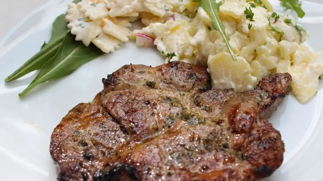 Saftiges Nackensteak grillen mit Kartoffel- und Nudelsalat auf einem weißen Teller.