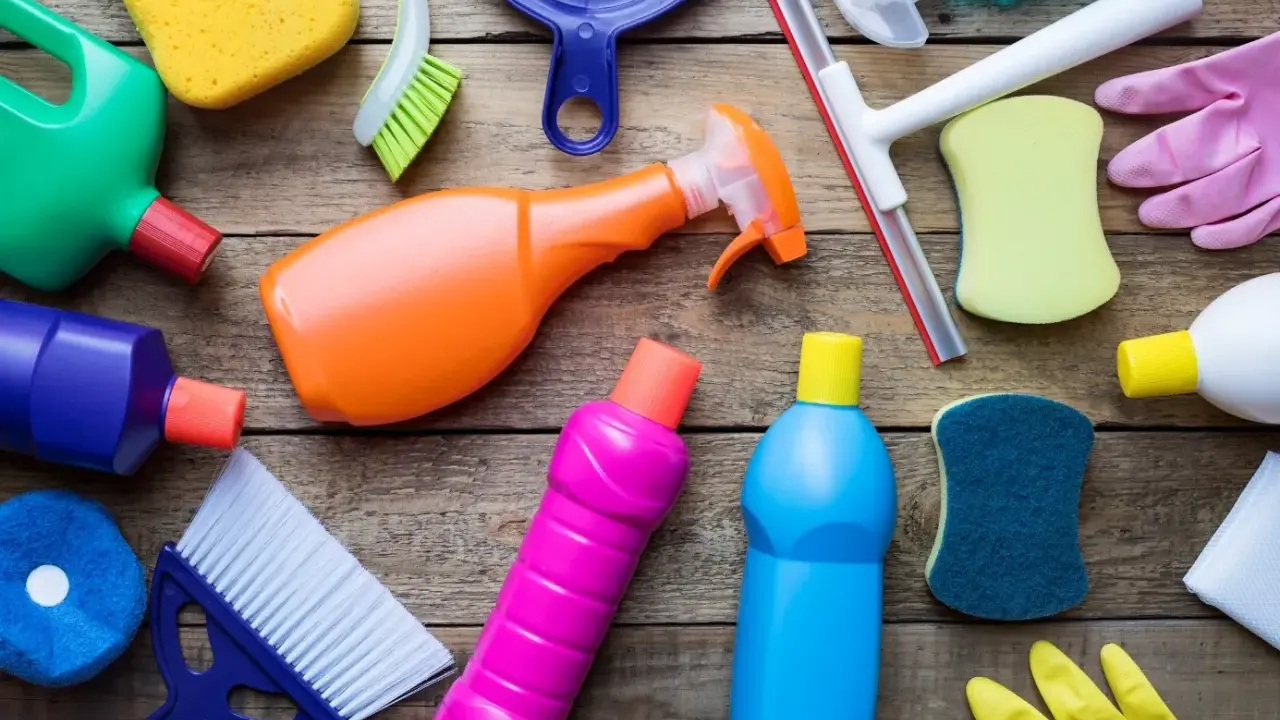 Divers produits et accessoires de nettoyage colorés sur fond de bois.