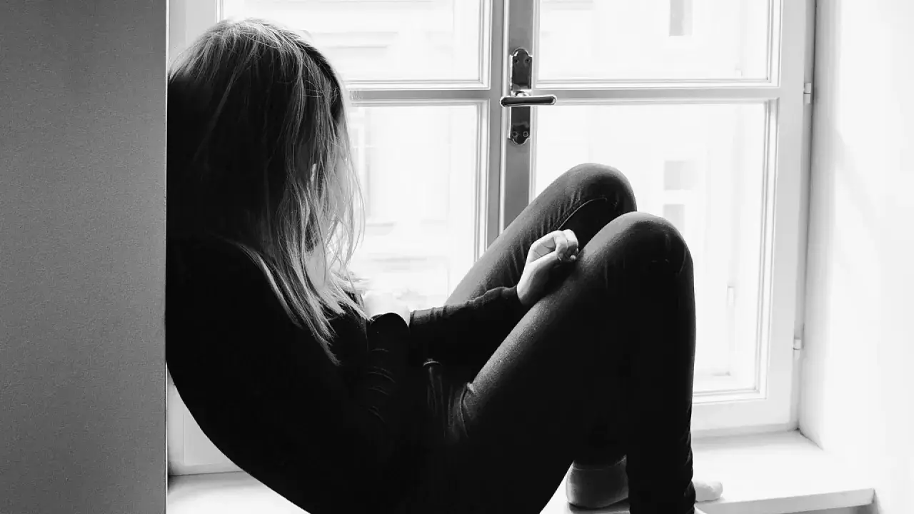Una joven sentada en la ventana, con la mirada perdida. Un momento para reflexionar sobre qué decirle a tu hija cuando le rompen el corazón.