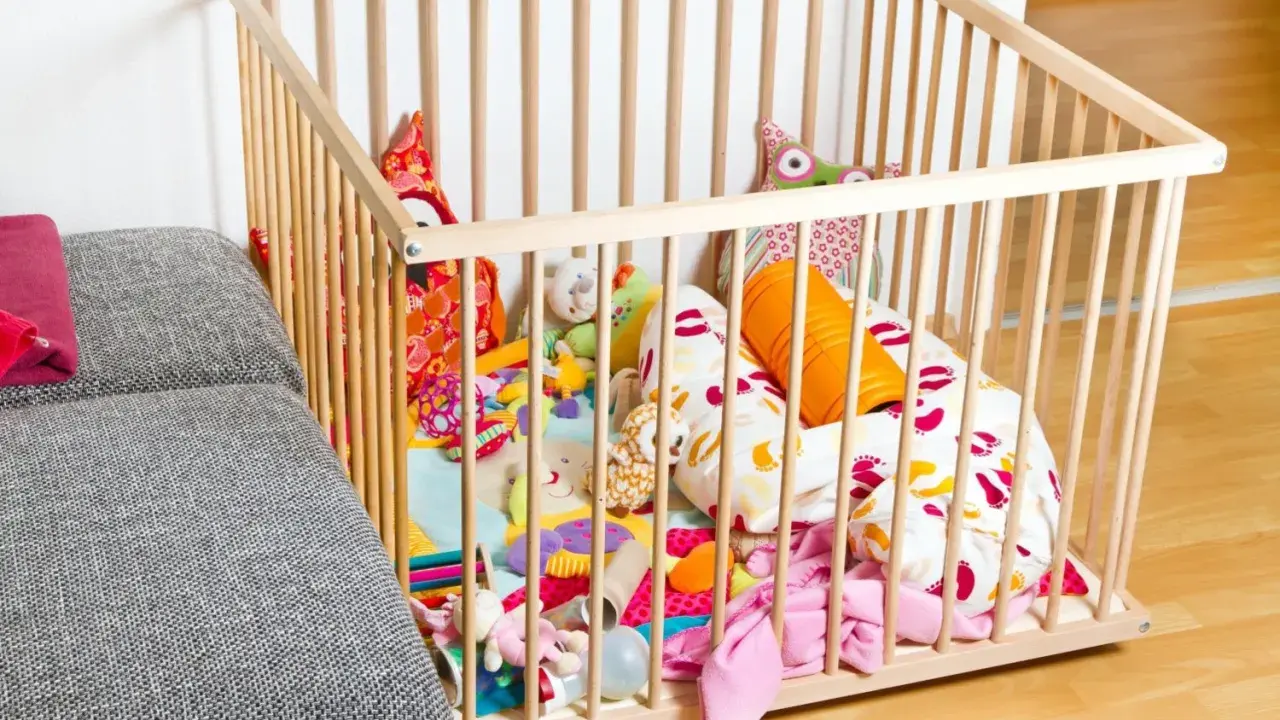 Ein bunter Spielteppich mit vielen Kuscheltieren und Kissen in einem Laufstall. Ja oder nein, diese sichere Spielzone für Babys?