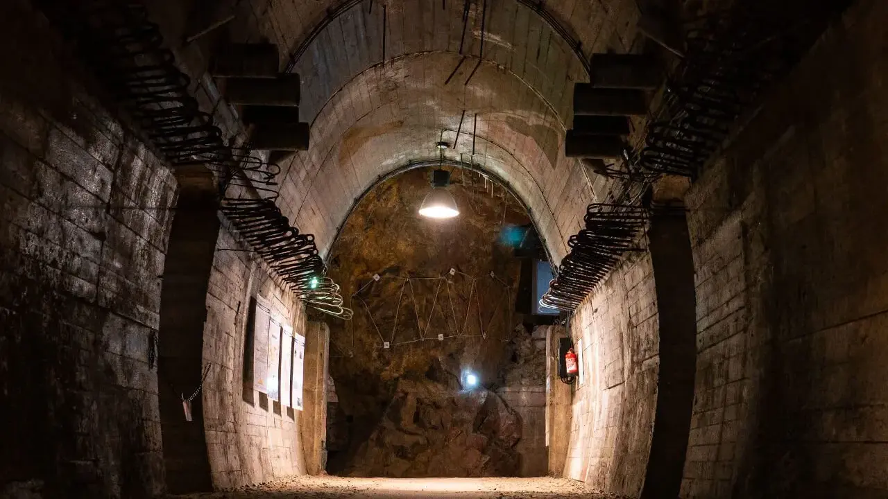 Wnętrze tunelu w Górach Sowich. Betonowe ściany, łukowe sklepienie i skalna grota z instalacją świetlną.
