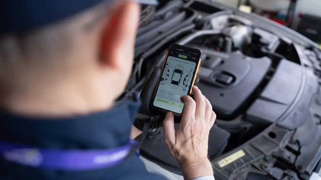 Mechanik sprawdza na telefonie raport z pomiaru lakieru i szczelin, szukając potencjalnych **kody błędów** w samochodzie.