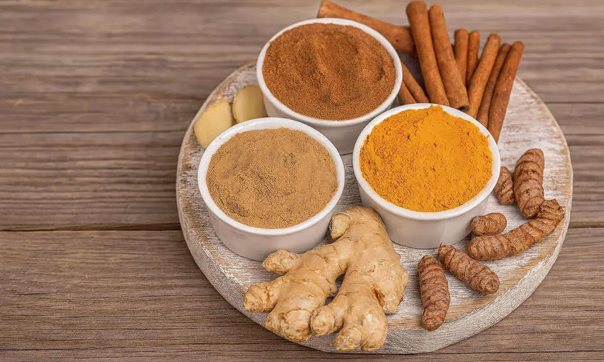 Poudre de curcuma, gingembre frais et bâtons de cannelle sur une planche en bois. Idéal pour un thé réconfortant au curcuma et miel.
