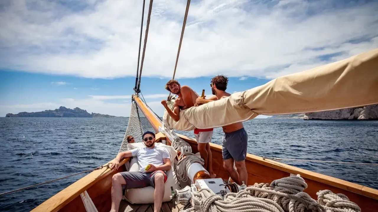 Trois amis profitent du soleil sur un voilier, rêvant d'un tour du monde. L'eau bleue et les falaises en arrière-plan ajoutent à l'aventure.