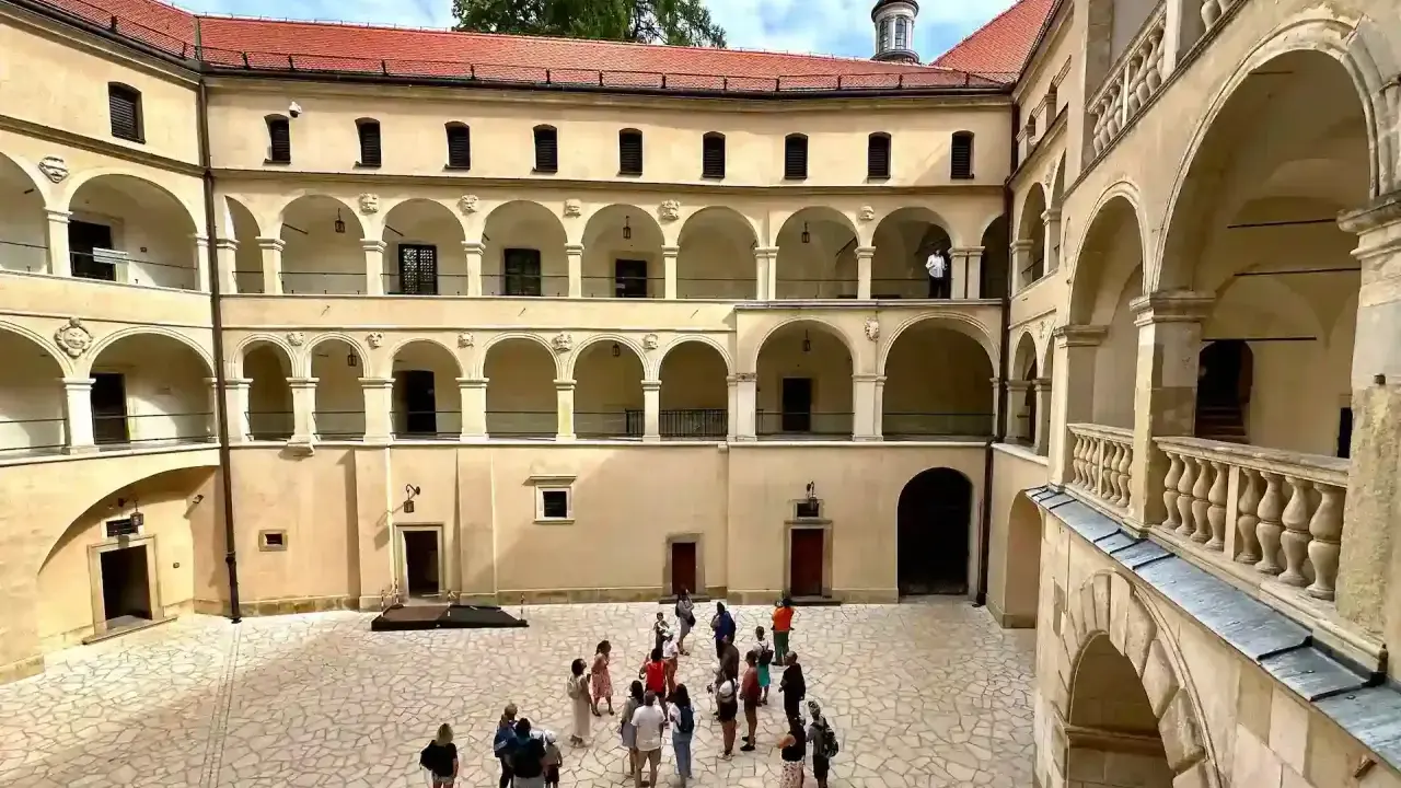 Dziedziniec zamku w Ojcowie z arkadowymi krużgankami i grupą turystów.