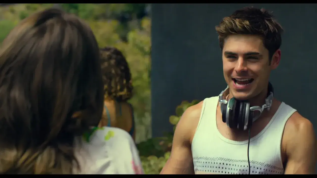 Il cast di We Are Your Friends, Zac Efron con le cuffie al collo, sorride mentre parla con qualcuno fuori campo.