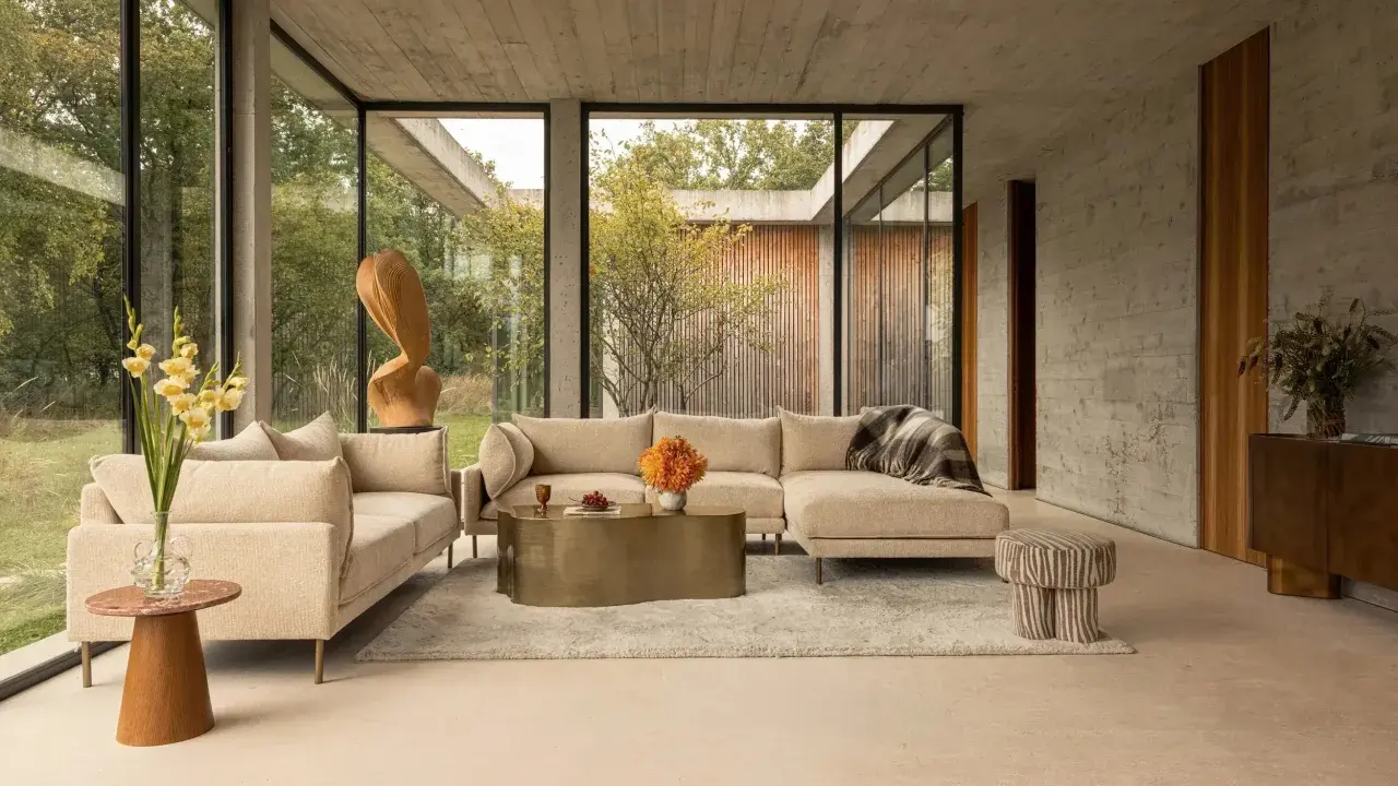Un salon moderne avec un canapé beige, une table basse dorée et des touches de couleur orange et verte. Une question se pose : quelle couleur assortir avec le beige pour un intérieur chaleureux ?