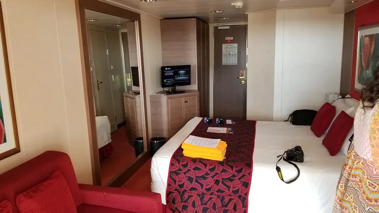Cabina MSC Musica con letto, divano rosso, specchio e TV. Perfetta per una vacanza in crociera.
