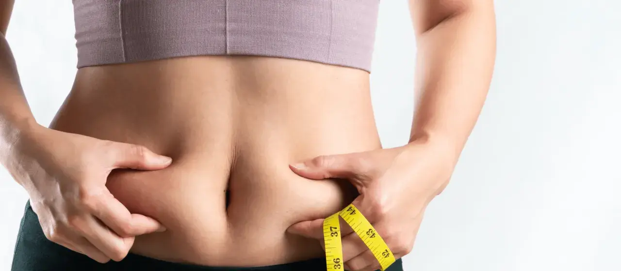 Frau kneift Bauchfett, Maßband zeigt Umfang. Tipps für 10 Hausmittel gegen Bauchfett.
