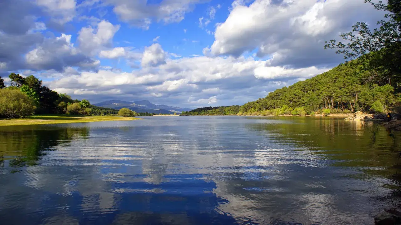 El embalse La Jarosa, con su agua serena reflejando el cielo nublado y rodeado de verdes colinas, invita a la calma.
