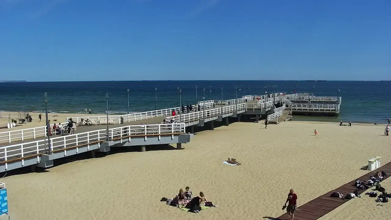 Słoneczny dzień na gdańskiej plaży Brzeźno. Ludzie spacerują po molo, odpoczywają na piasku, ciesząc się widokiem morza.