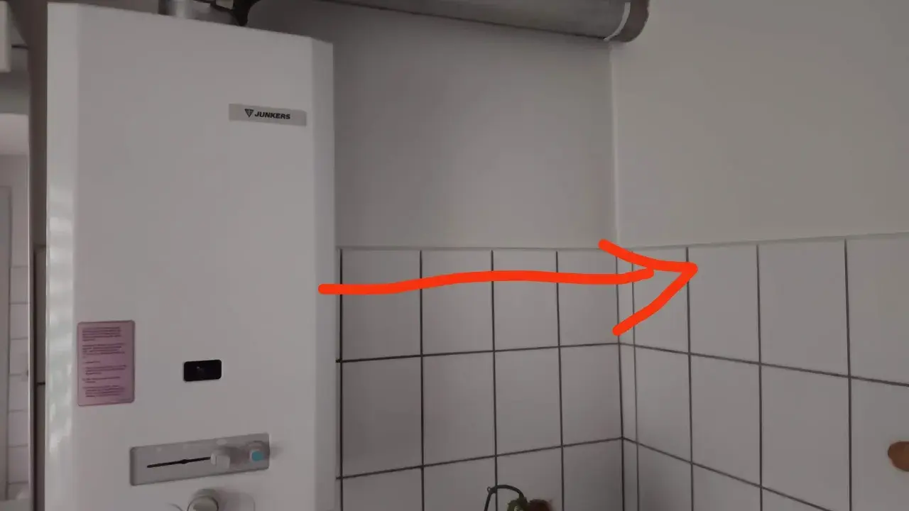 Ein Junkers-Durchlauferhitzer mit Gasflasche ist an der Wand montiert. Ein roter Pfeil zeigt auf die Ecke.