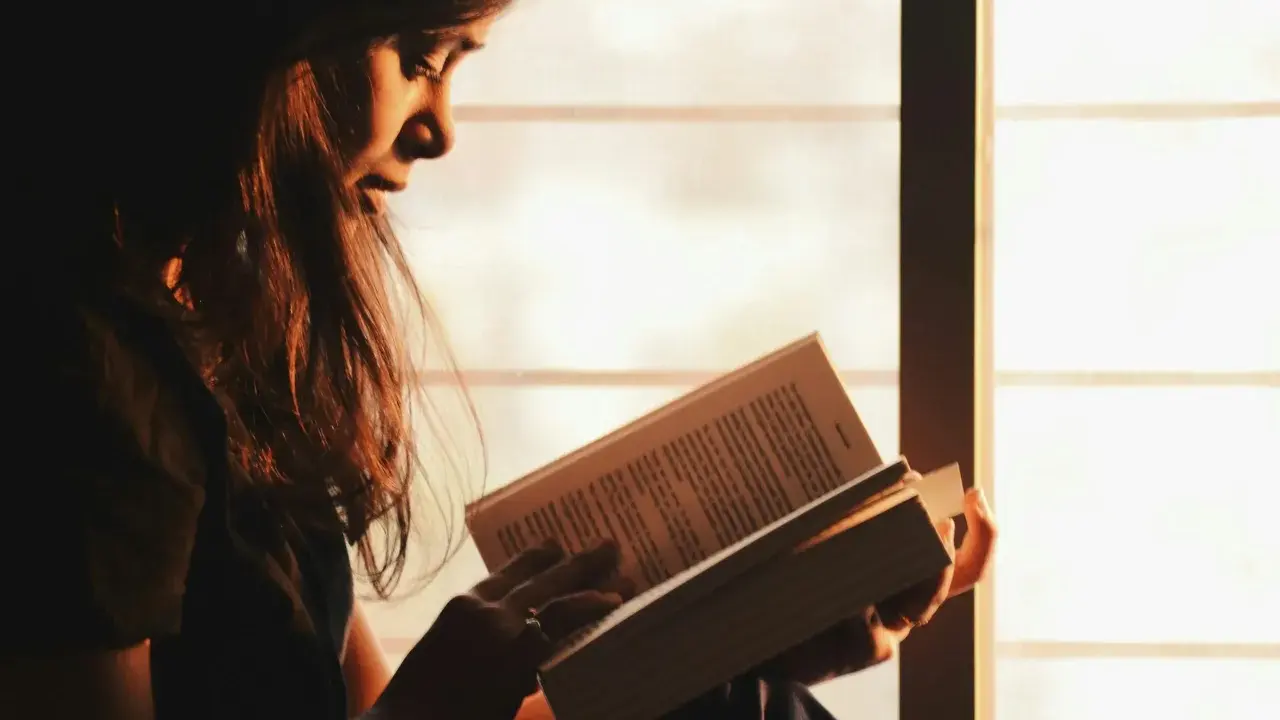 Ragazza immersa nella lettura, illuminata dalla luce dorata del tramonto, sfoglia pagine che potrebbero contenere i libri di Emmanuel Carrère.