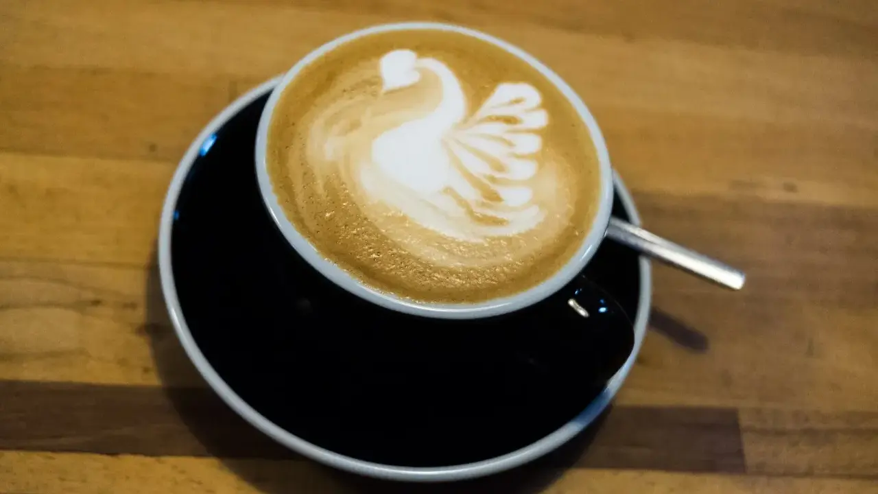 Cappuccino mit Milch-Schwan-Latte-Art auf schwarzer Untertasse. Perfekt für jeden Kaffeeliebhaber.