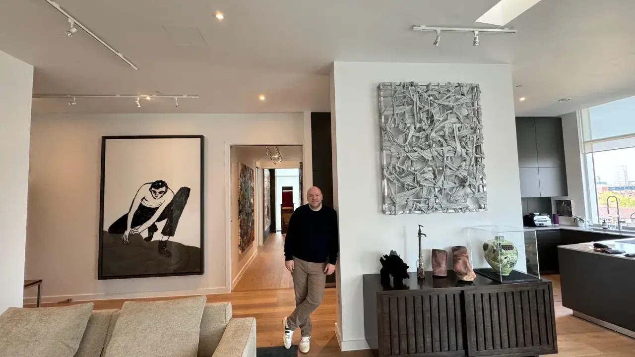Guy Hepner stands in a modern apartment filled with art, including a large black and white drawing and a textured sculpture.