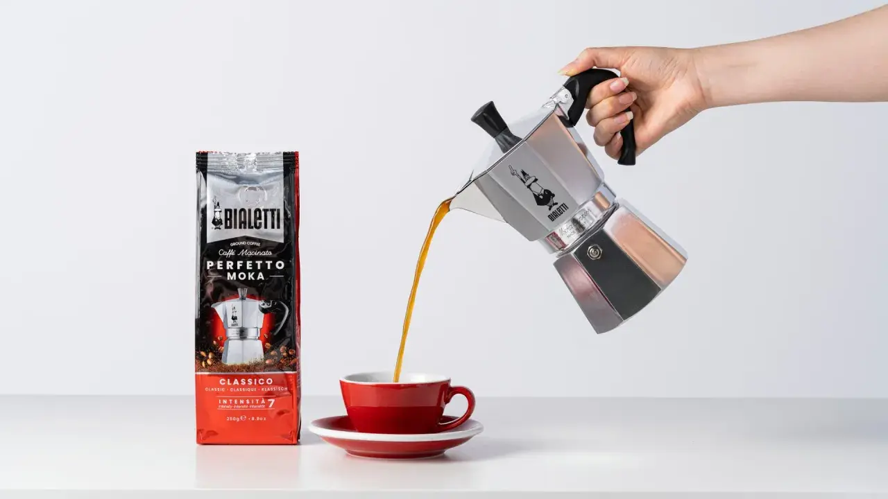 Popularna kawa Bialetti Moka wylewa się z kawiarki do czerwonej filiżanki.