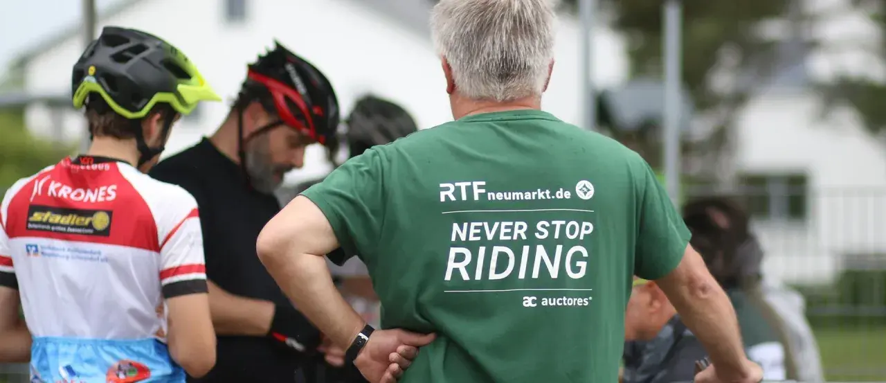 Männer in Radlerkleidung, einer trägt ein grünes T-Shirt mit der Aufschrift "RTFneumarkt.de NEVER STOP RIDING".