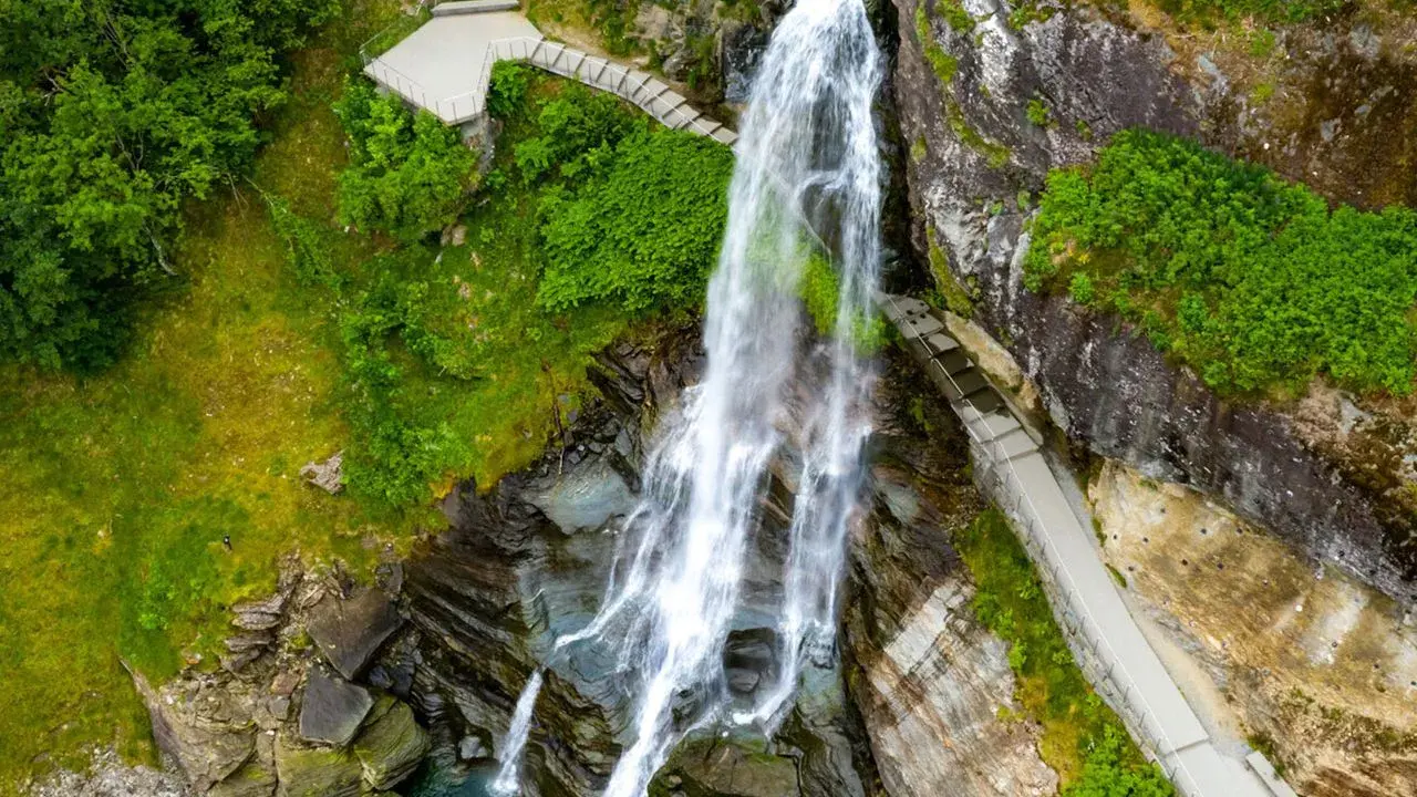 Majestätischer norwegischer Wasserfall stürzt in ein türkisfarbenes Becken. Wege führen Besucher nah heran.