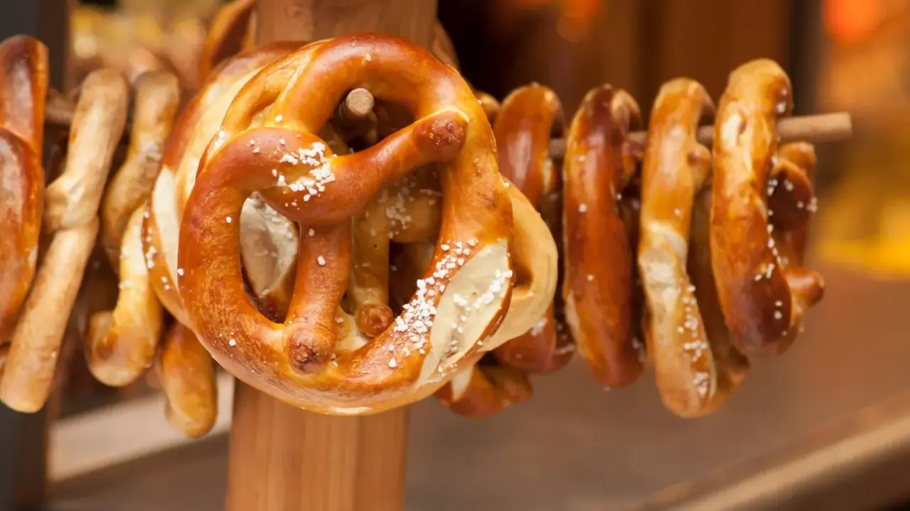 Des bretzels dorés, saupoudrés de gros sel, sont suspendus sur un support en bois. Ces spécialités lorraines invitent à la dégustation.