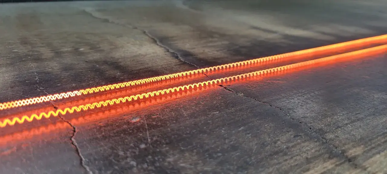Dos espirales incandescentes, demostrando el efecto Joule en una caldera, brillan con un naranja intenso sobre una superficie oscura y agrietada.