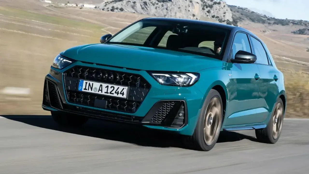 Audi RS1 verde azulado en movimiento por una carretera rural con montañas al fondo.