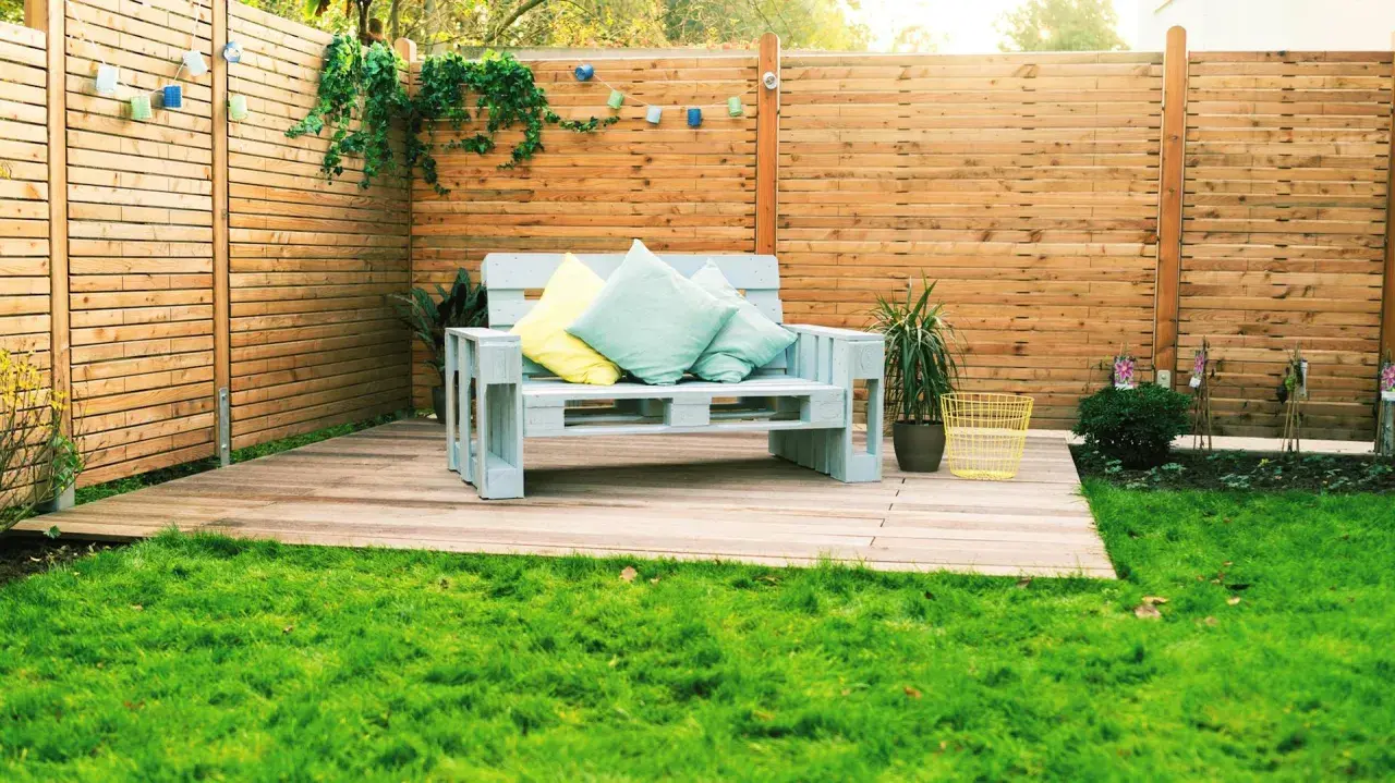 Ein gemütliches Palettensofa bauen: Ein hellblaues Sofa aus Paletten mit Kissen steht auf einer Holzterrasse im Garten.