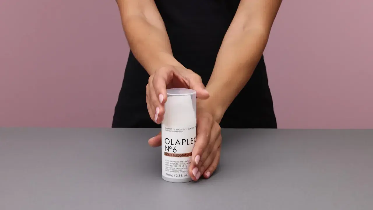 Hände halten eine Flasche Olaplex Nr. 6 Bond Smoother, ein Leave-in Styling Treatment für Feuchtigkeit und Stärke.